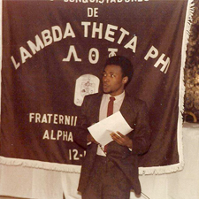 Ramiro Metos Aviles, Jr. stands in front of a Lambda Theta Phi banner